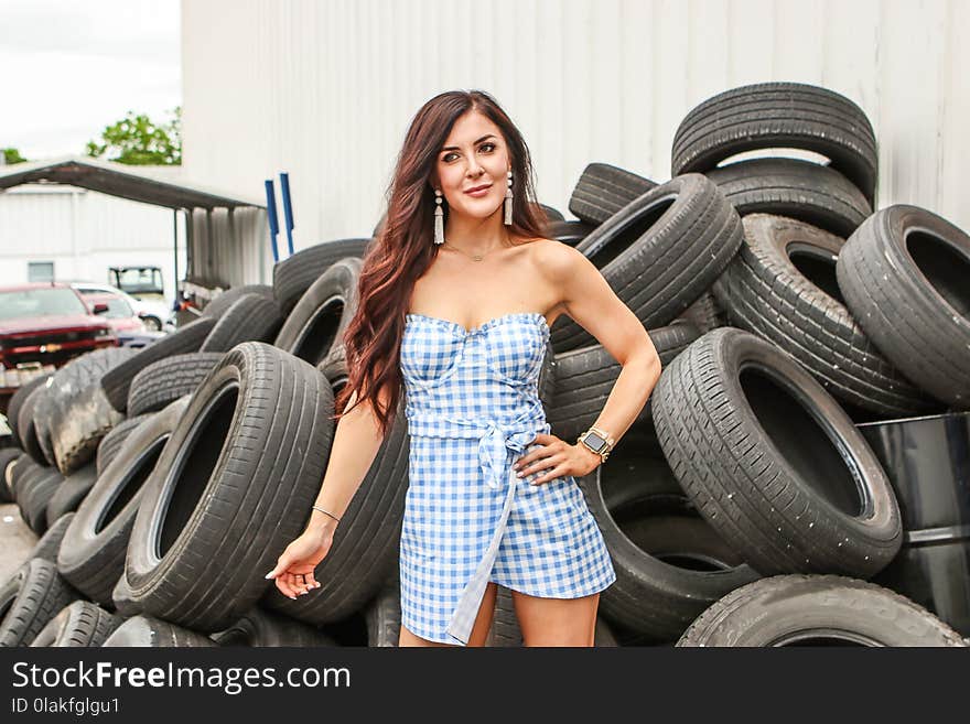 Woman in Blue and White Checkered Dress Standing in Front of Stack Tires