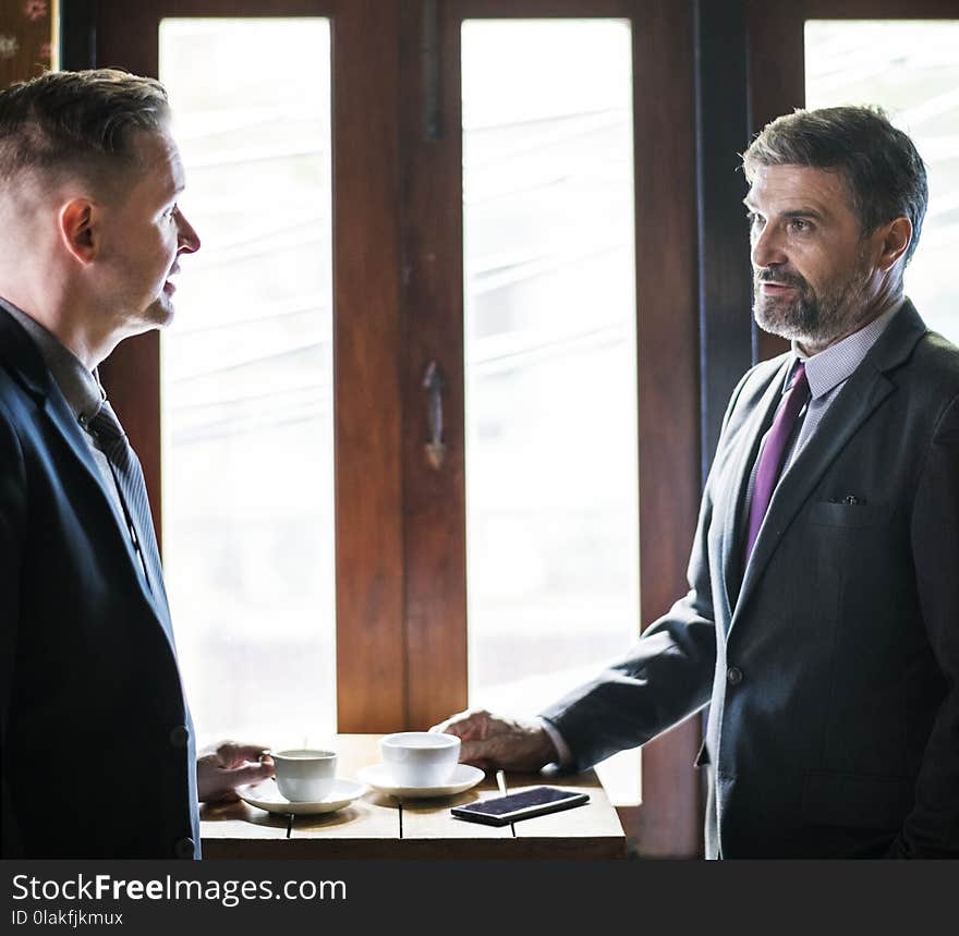 Two Person Talking in Front of Brown Wooden Table With Cup of Coffees