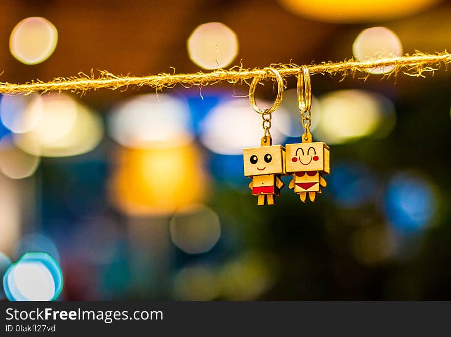 Two Man and Woman Wooden Couple Keychains Hanging on Rope Overlooking Bokeh Lights