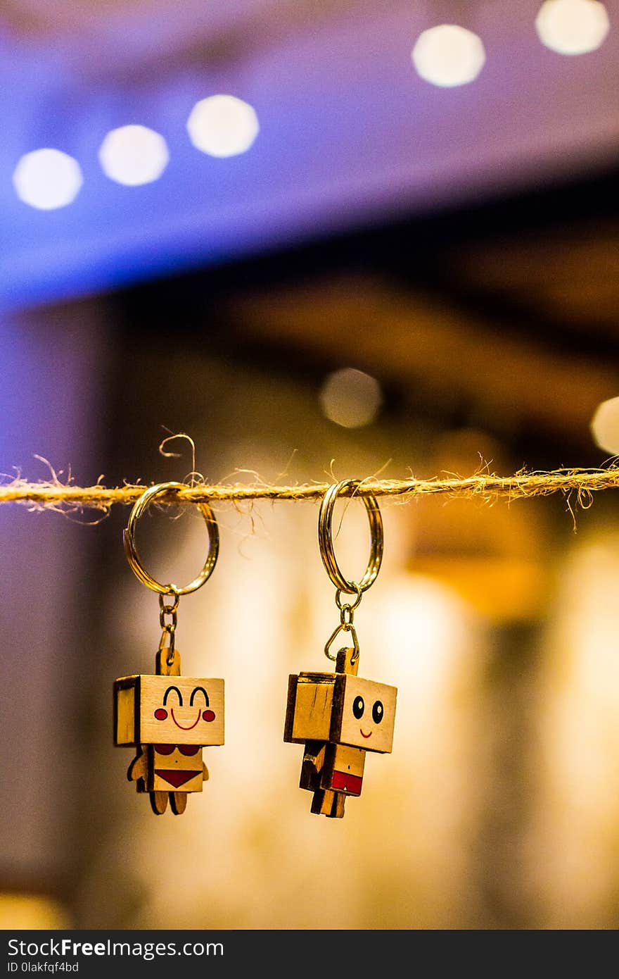 Bokeh Photography of Two Wood Block Man and Woman Figure Key Chains Hanging on Brown Thread