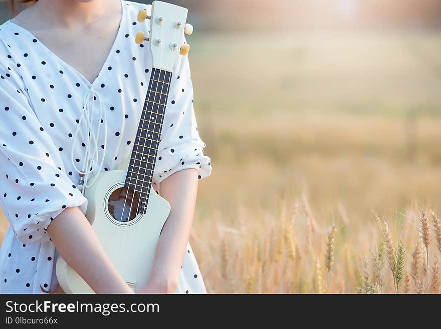 Beautiful asian woman playing ukulele and relaxing at barley field in summer on sunset time.