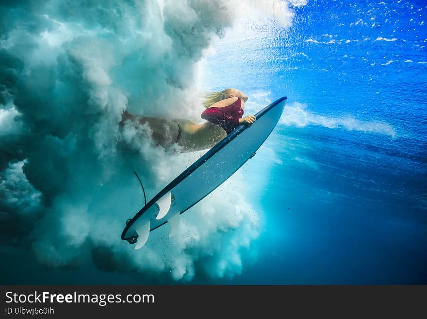 Surfer girl under wave against blue colored sea water surface. Surfer girl under wave against blue colored sea water surface