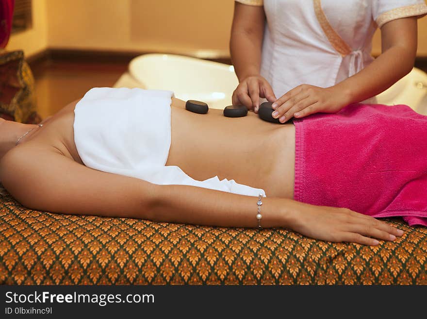 Beautiful woman having hot stones on her belly in spa salon. Concept of healthcare and female beauty. Masseuse doing back massage with hot black stones close up