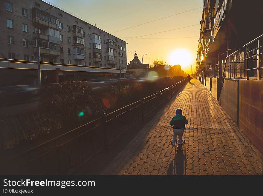 The boy rides a scooter towards the movement. The sun sets over the horizon.