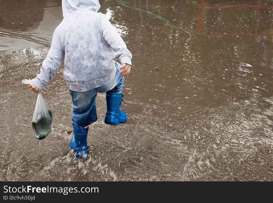 Little boy running around the puddles.