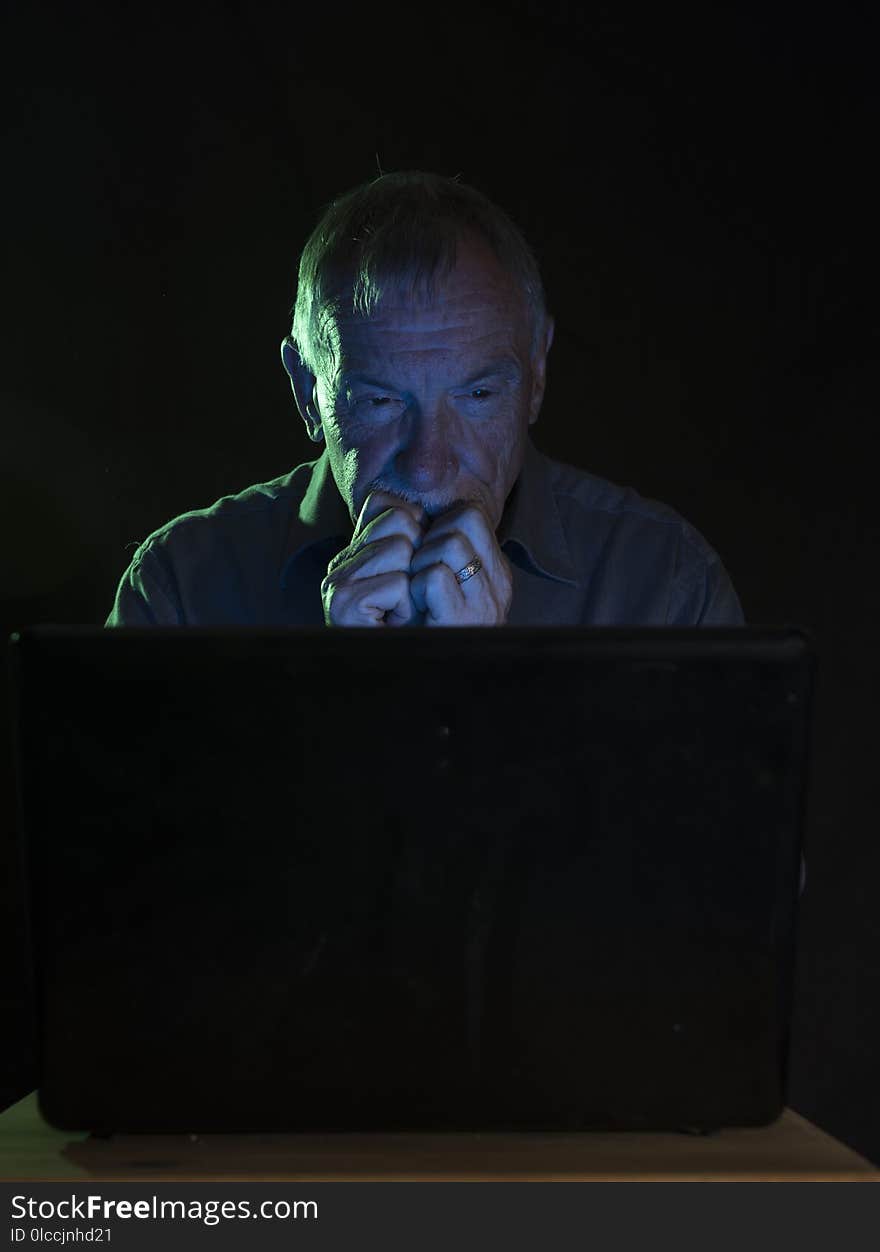 Serious senior man looking at a computer screen at night