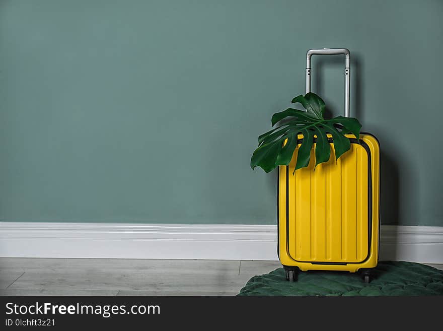 Bright yellow suitcase with tropical leaf near color wall indoors