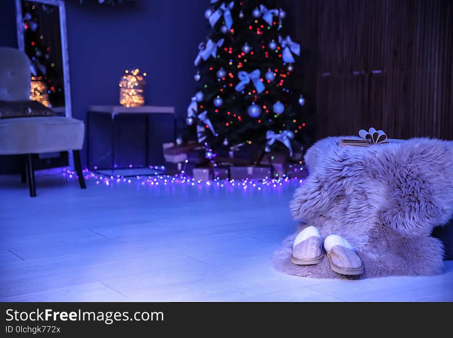 Soft slippers with fluffy blanket and Christmas tree in dark room