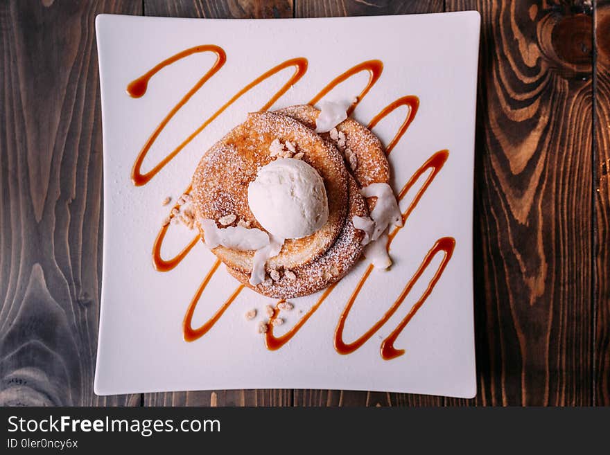 Top view of Pancakes topping with a scoop of coconut ice cream, coconut meat, crispy rice and icing over caramel lines on white plate.