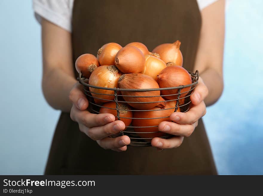 Woman holding basket with ripe onions on color background