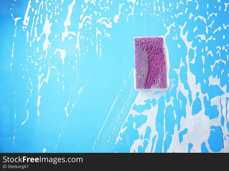 Sponge on glass covered with suds against color background