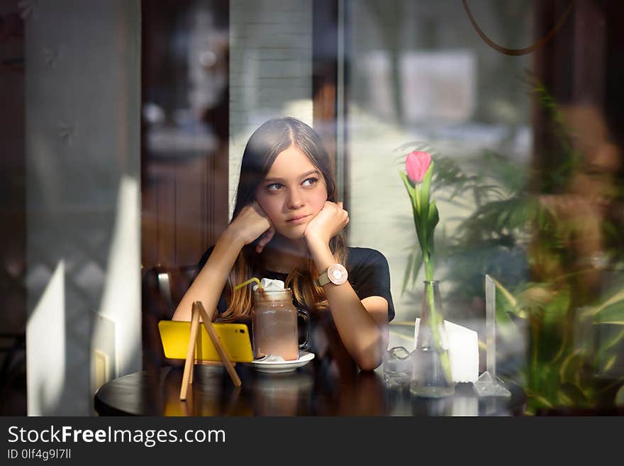 Pensive girl sitting in a cafe on the table is a pink tulip. Pensive girl sitting in a cafe on the table is a pink tulip