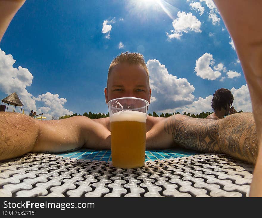 Beautiful young man enjoying beer at the pool outside