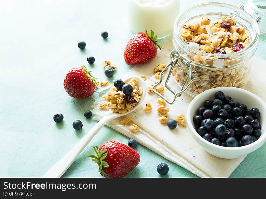 Glass jar of homemade granola with coconut chips,nuts and dry cranberry on turquoise wooden background.