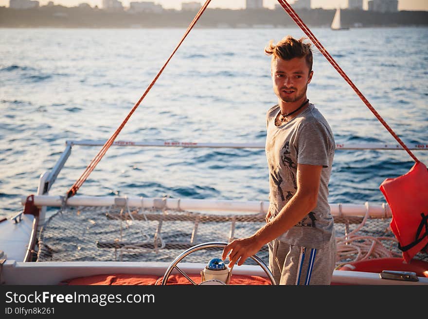 Young handsome man, captain driving yacht in sea at sunny day.