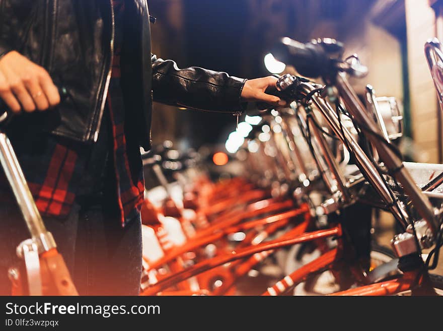 Young girl in black leather jacket using bike on background illumination glow bokeh light in night atmospheric city, hipster biking and riding to work by bicycle on urban street, ecology concept