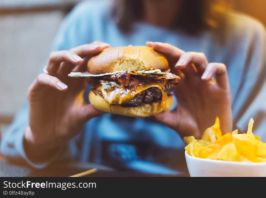 Young girl holding in female hands fast food burger, american unhealthy calories meal on background, mockup with copy space for text message design, hungry human with grilled hamburger front view