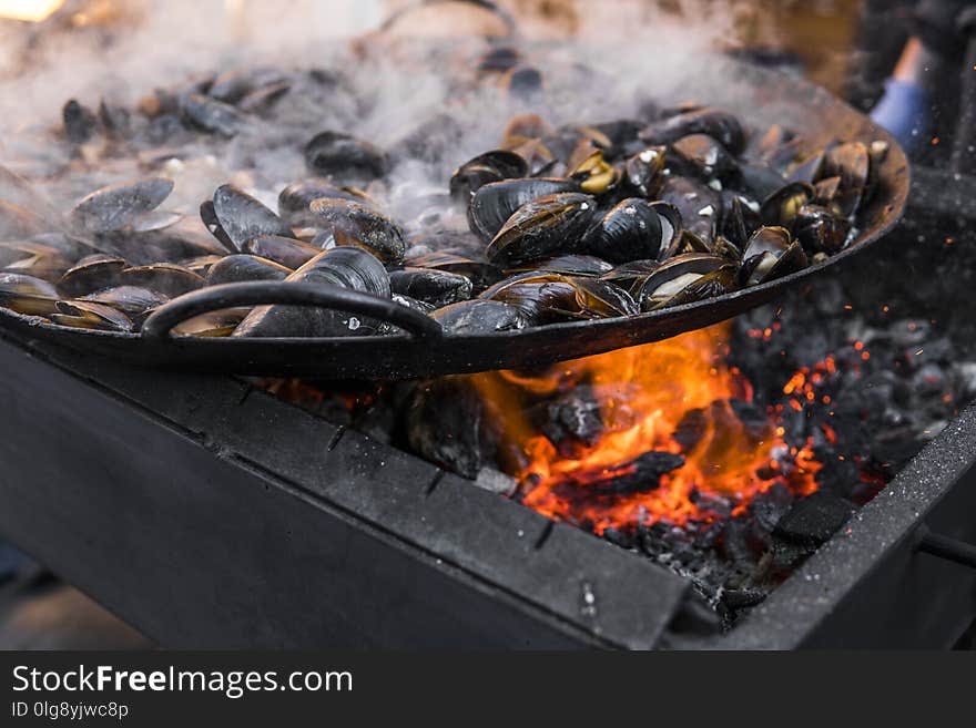 Fresh mussels at grill pan. Seafood barbecue outdoors. Picnic healthy food, mussels in shells. Plenty of mussel shells cooking at large metallic pan