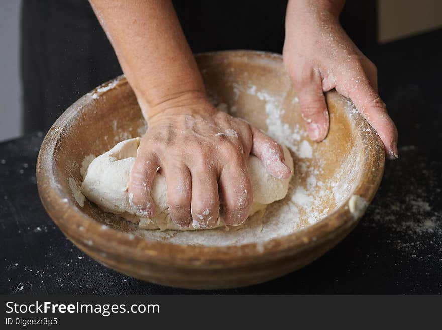 Slow motion shot of baker hands kneading dough in flour in wooden bowl