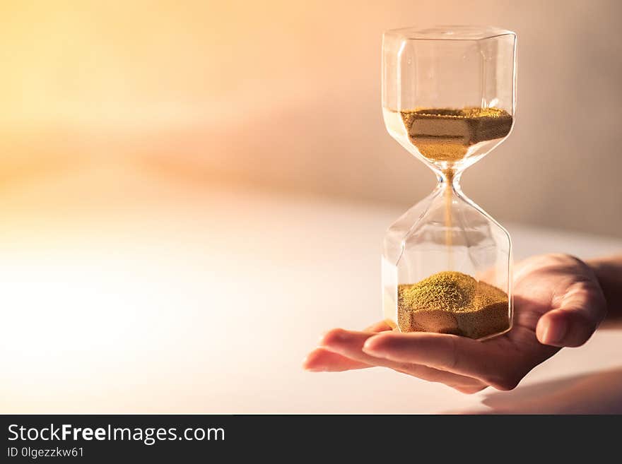 Close up of brown sand running through the shape of modern hourglass on male hand.Time passing and running out of time. Urgency countdown timer for business deadline concept with copy space. Close up of brown sand running through the shape of modern hourglass on male hand.Time passing and running out of time. Urgency countdown timer for business deadline concept with copy space