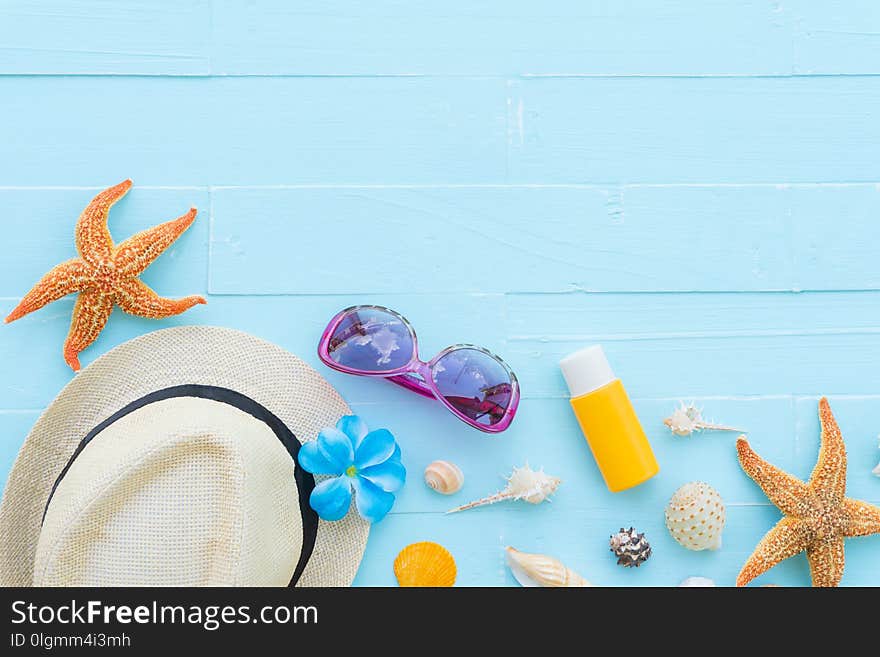 Beach accessories including sunglasses, starfish, hat beach, sunblock, colorful flip flop and shell on bright blue pastel wooden background for summer holiday and vacation concept.