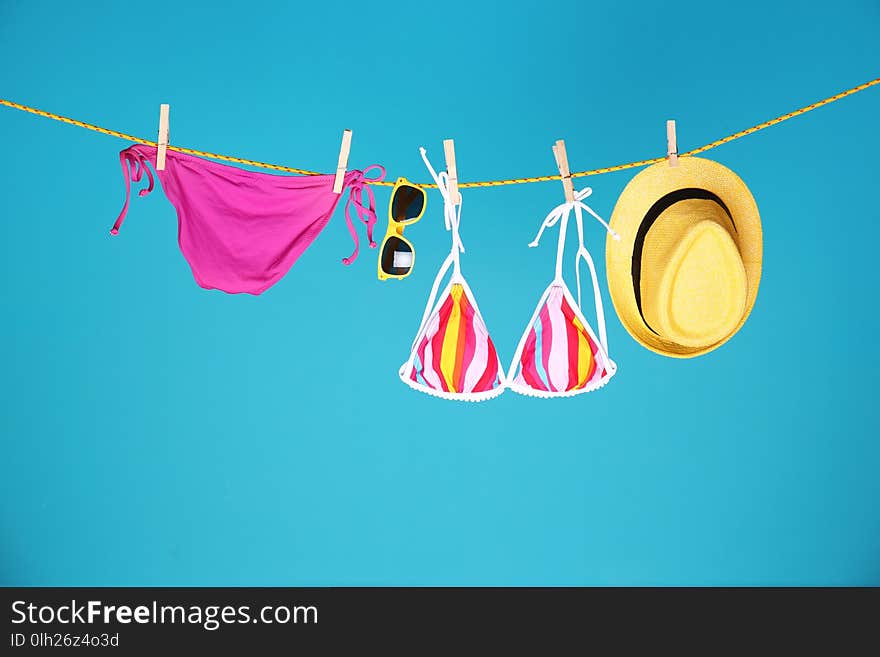 Beautiful bikini, hat and sunglasses hanging on rope against color background