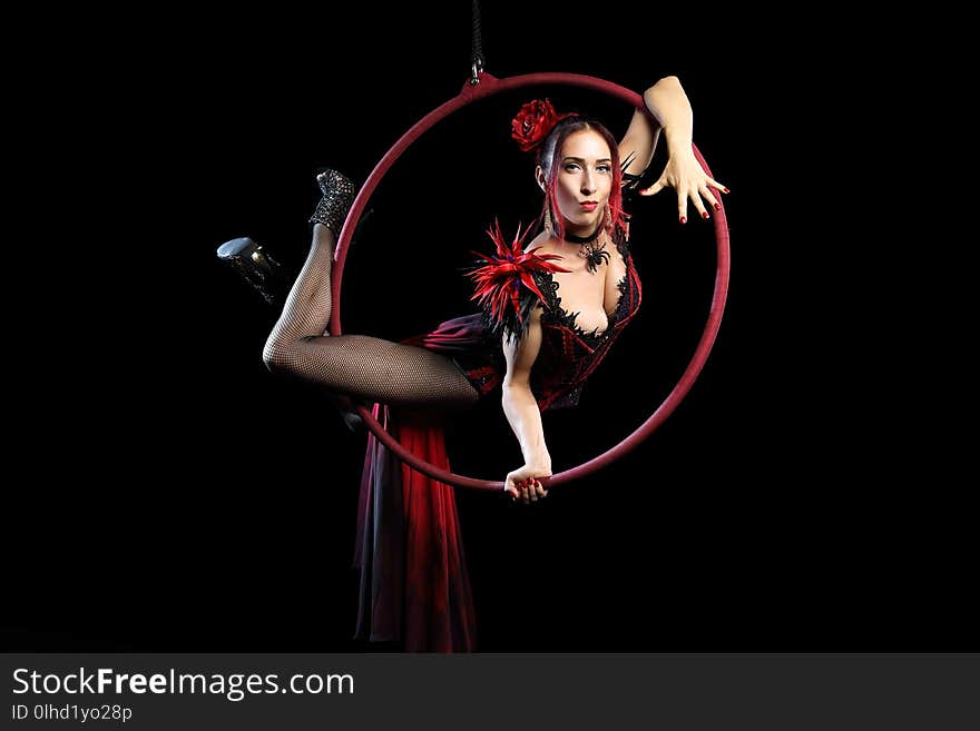 Acrobatic woman in beauty long and red dress and in hills doing element on aerial hoop isolated on black background. Acrobatic woman in beauty long and red dress and in hills doing element on aerial hoop isolated on black background