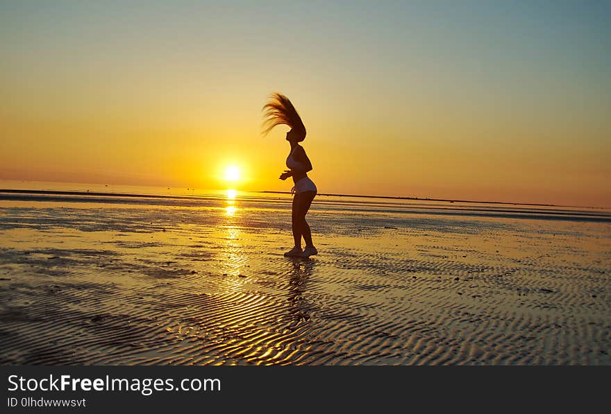 Silhouette flexible gymnastics girl on the shore of Sea during twilight.