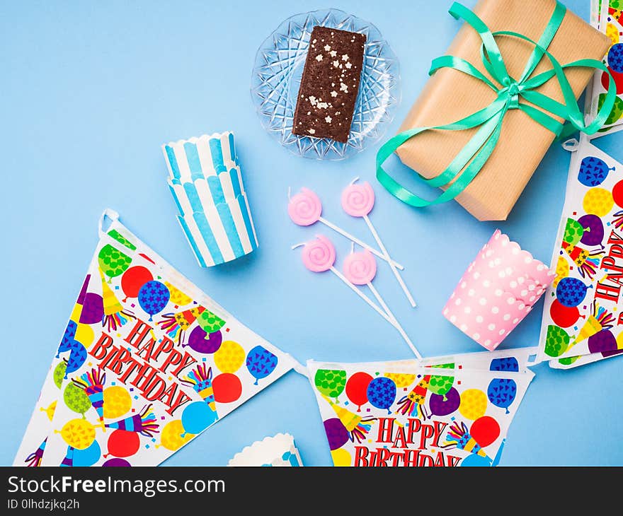 Happy Birthday party items flat lay. Candles, gift box, decoration banner, paper glasses, chocolate cake