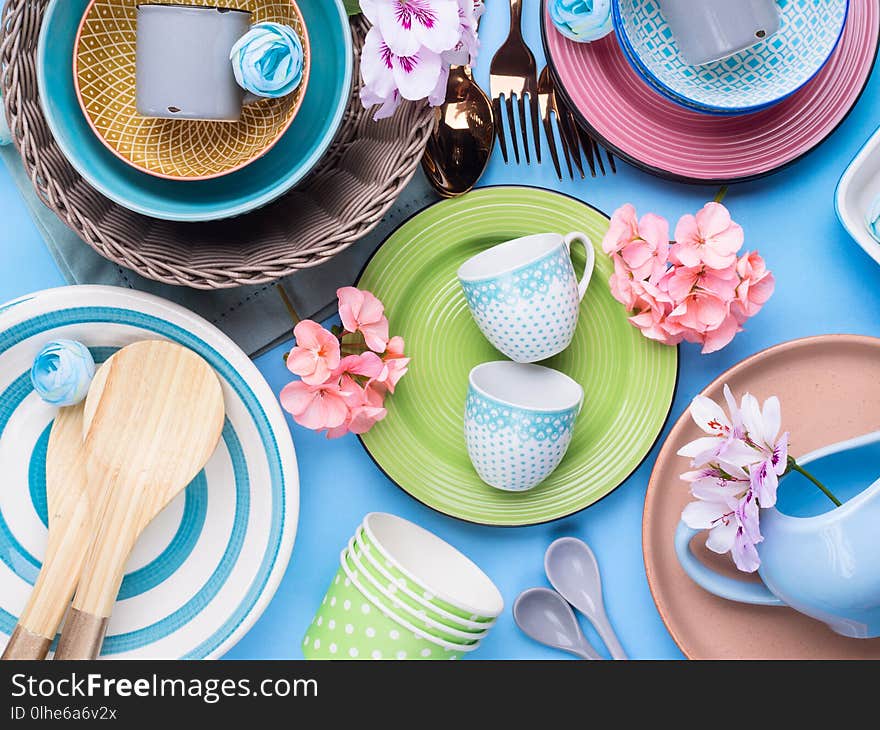 Tableware dish set on blue pastel background with flowers. Flat lay