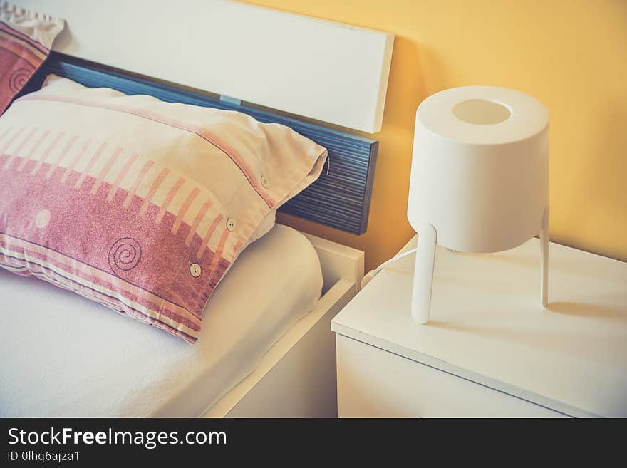 White lamp on night table next to the bed in modern hotel bedroom. Cozy living concept. Close up. White lamp on night table next to the bed in modern hotel bedroom. Cozy living concept. Close up.