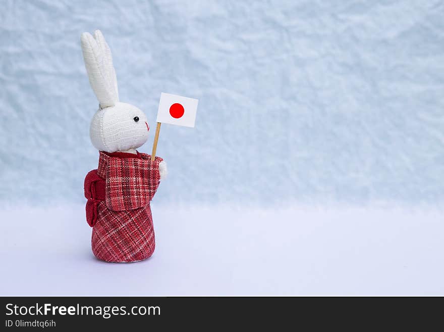 Fabric rabbit doll in red traditional Japanese dress holding Japan flag over blurred background