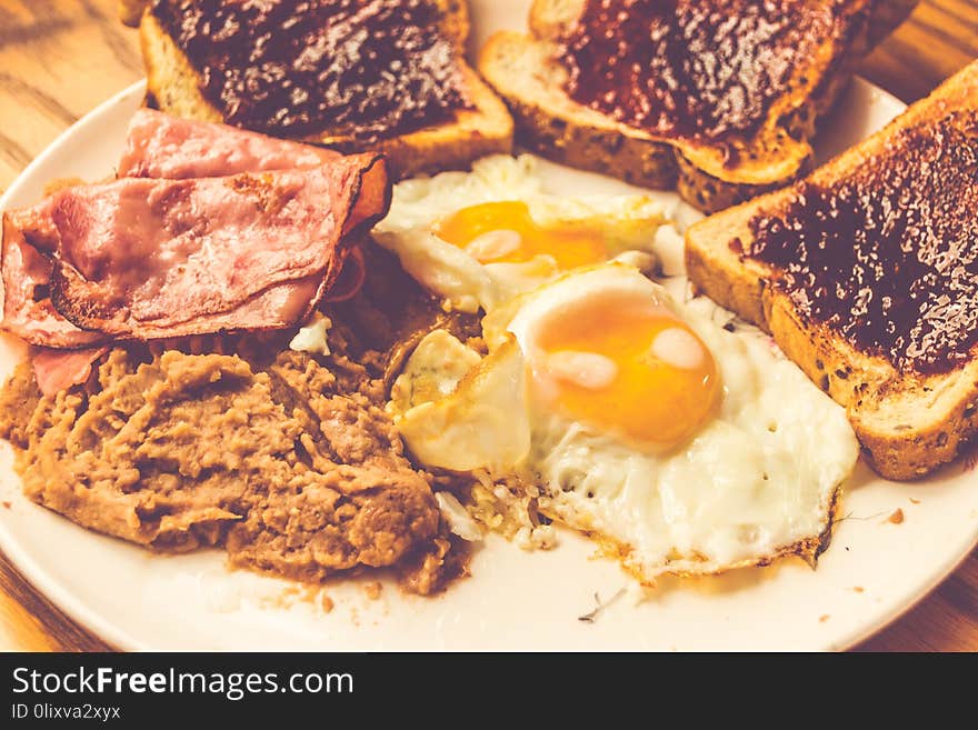 Photograph of a plate with fried eggs, beans, ham and bread. Photograph of a plate with fried eggs, beans, ham and bread