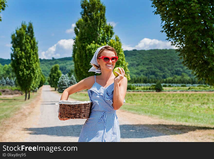 Happy woman in dress with wicker basket is walking the road in the countryside