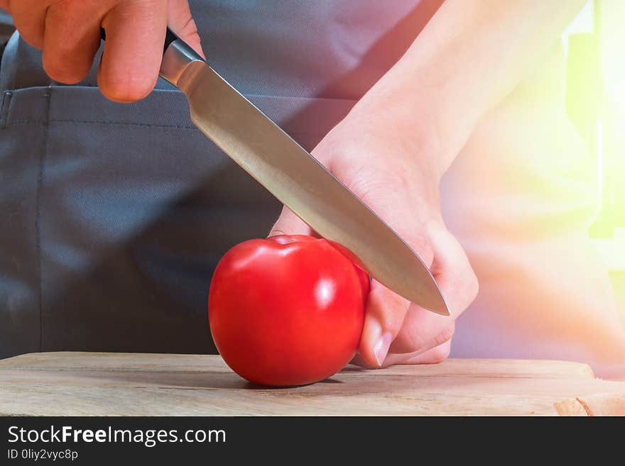 Female hands with knife cutting ripe red tomato on wooden board. Warm sunny patch of light.