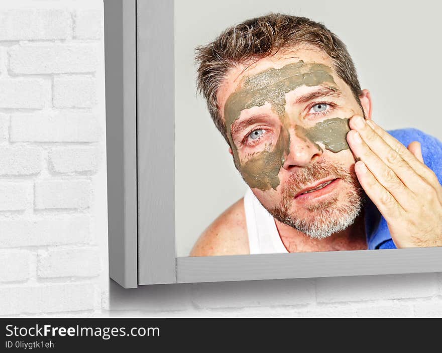 Lifestyle mirror portrait of young attractive and happy man with bathroom towel with green cream on his face applying facial mask in skin care beauty and male cosmetics use concept