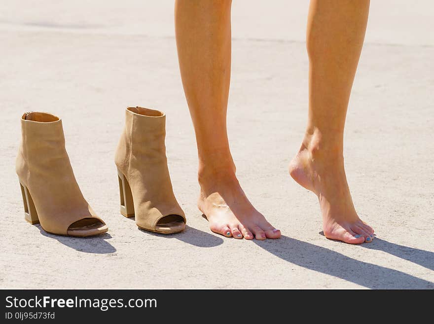 Barefoot unrecognizable woman standing next to beige brown high heels boot relaxing her feet after a long walk. Barefoot unrecognizable woman standing next to beige brown high heels boot relaxing her feet after a long walk.