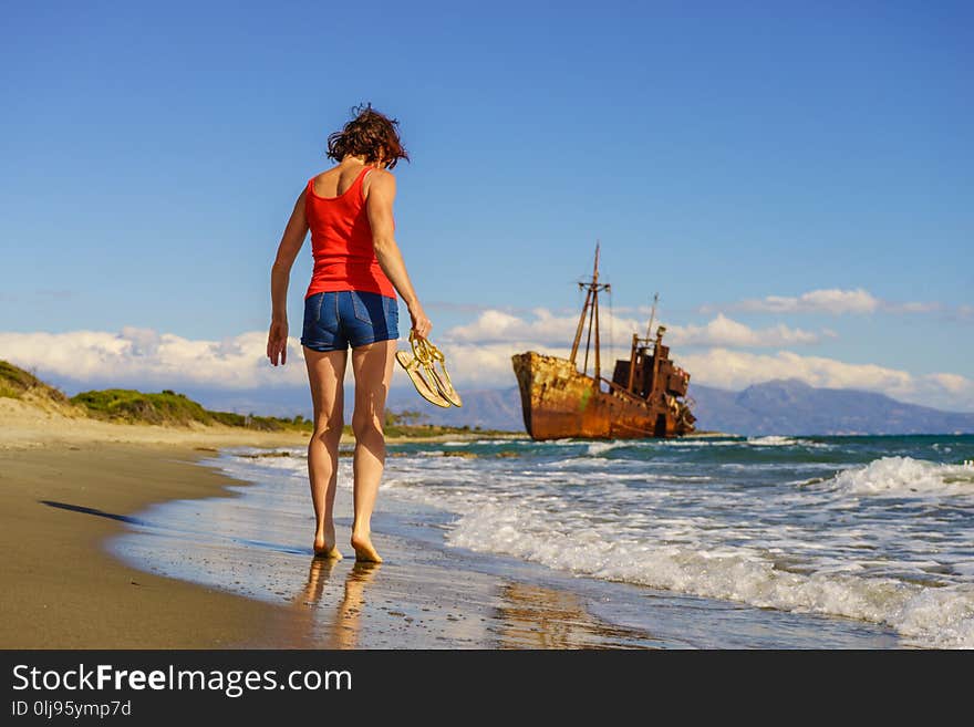 Travel freedom. Mature tourist woman walking on beach enjoying summer vacation. An old abandoned shipwreck, wrecked boat in the background. Travel freedom. Mature tourist woman walking on beach enjoying summer vacation. An old abandoned shipwreck, wrecked boat in the background