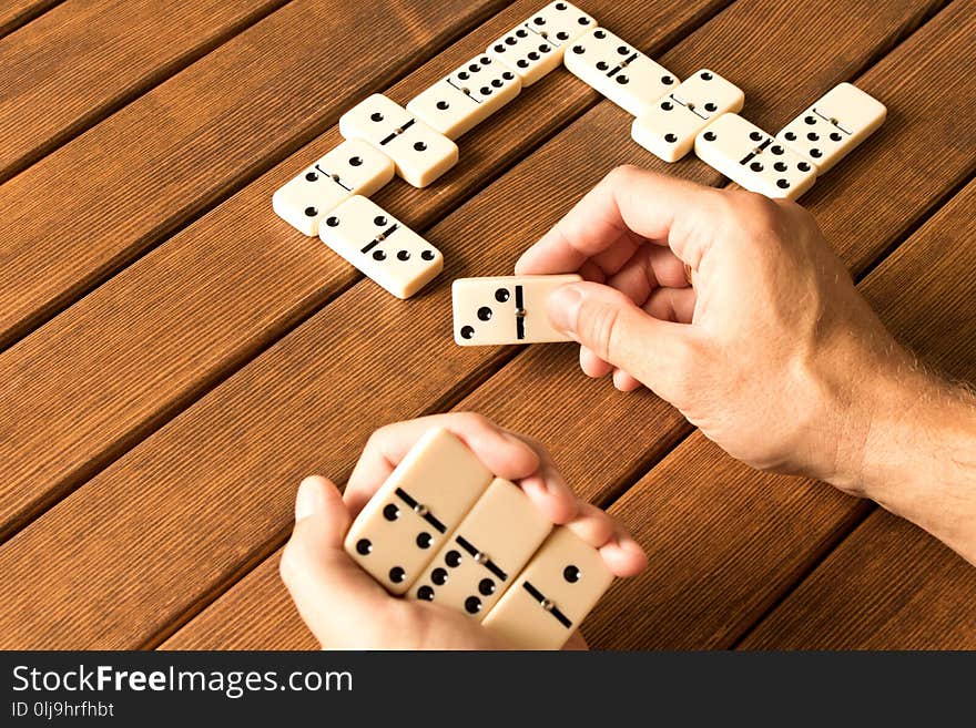 Playing dominoes on a wooden table. Man`s hand with dominoes