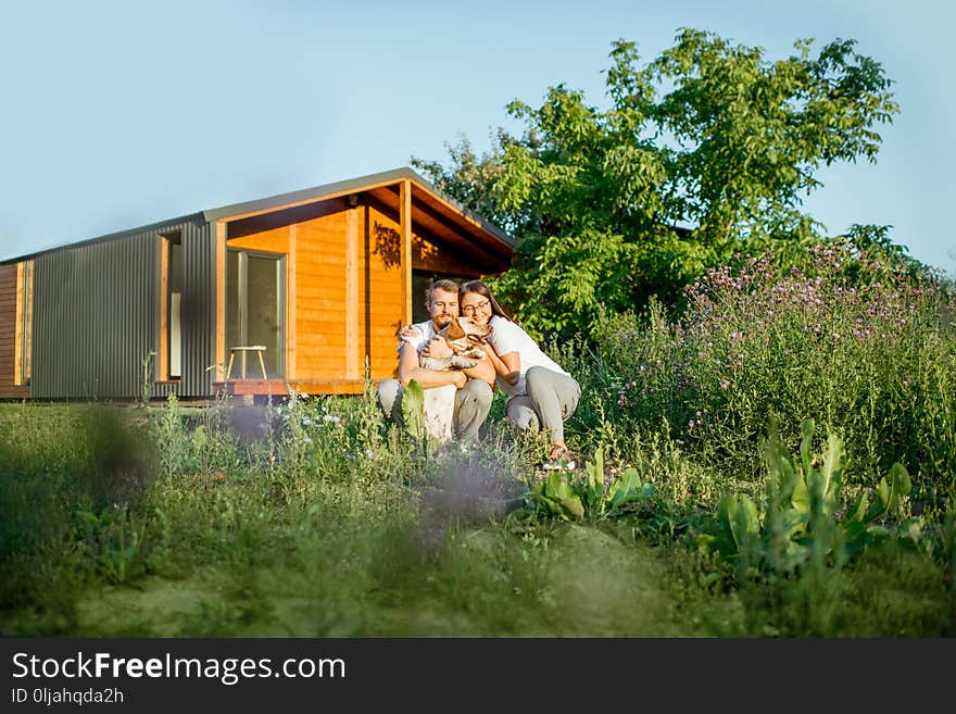 Young couple playing with dog on the backyard of the wooden country house during the sunset. Young couple playing with dog on the backyard of the wooden country house during the sunset