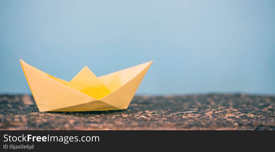 Yellow paper folded, origami, boat on a rock, blue background, copy space. Yellow paper folded, origami, boat on a rock, blue background, copy space