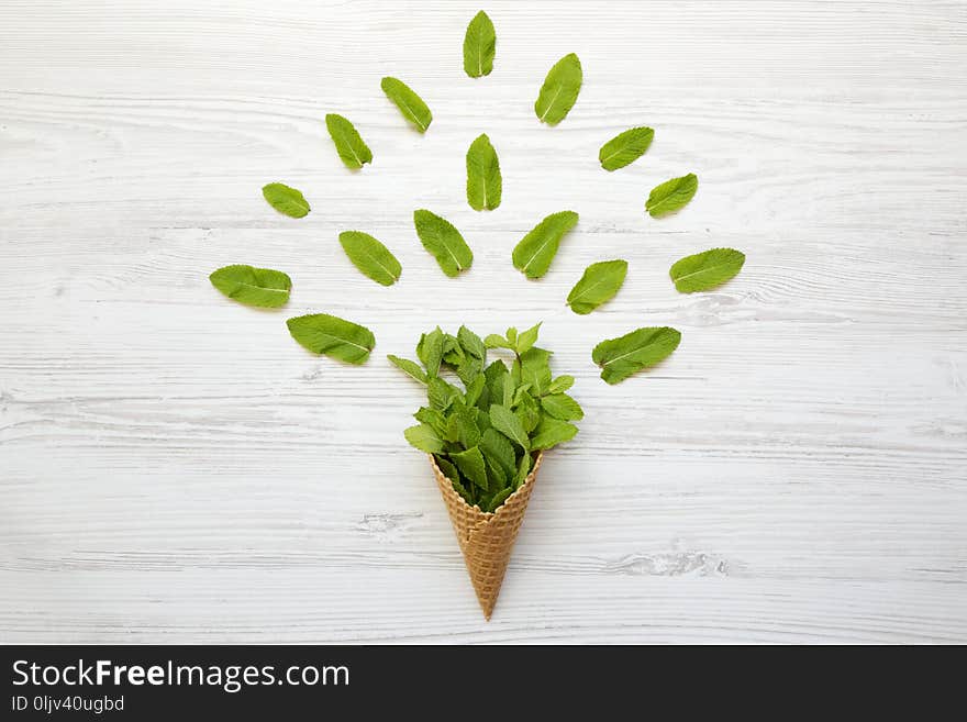 Waffle sweet cone with mint leaves over white wooden surface, top view. Flat lay, overhead. Summer background.