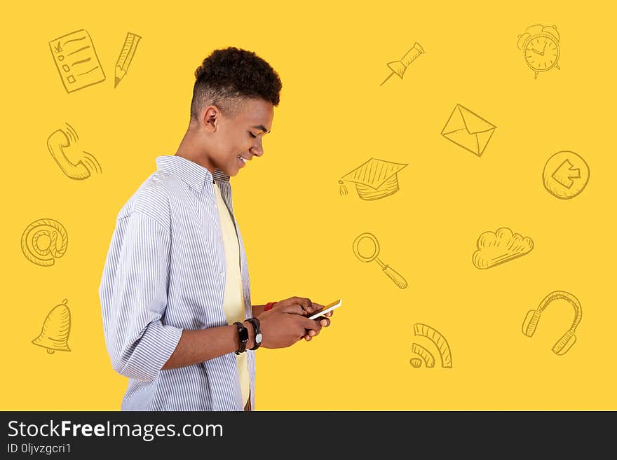 Typing messages. Cheerful popular blogger looking at the screen of his smartphone and smiling while writing messages to his followers. Typing messages. Cheerful popular blogger looking at the screen of his smartphone and smiling while writing messages to his followers