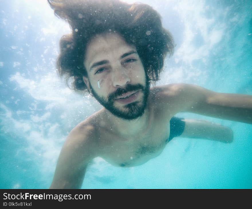 Attractive young man submerged in pool looking at camera