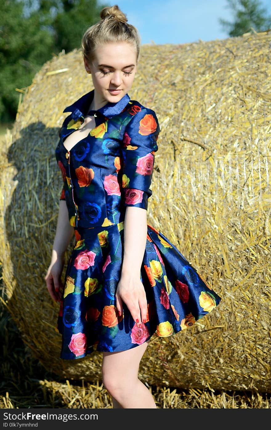 Female model, outdoor photo session, farmland in summer. Girl in colorful dress stands in front of roll of hay. Female model, outdoor photo session, farmland in summer. Girl in colorful dress stands in front of roll of hay.