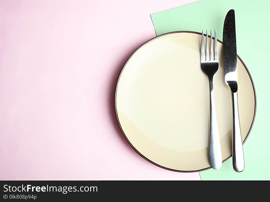 Plate, fork and knife on a pink and green background. Concept table setting. Top view