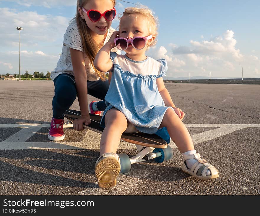 Street sports: two dvoichki in sunglasses sit on one large longboard in bright sunny weather. Close-up.