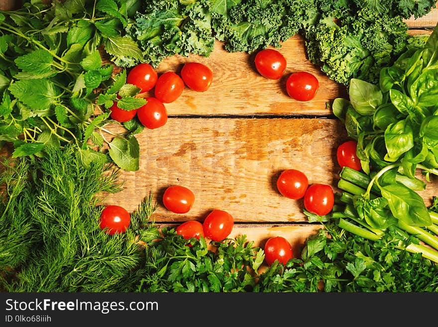 Background with green vegetables and herbs and tomatoes on a wooden table. Background with green vegetables and herbs and tomatoes on a wooden table