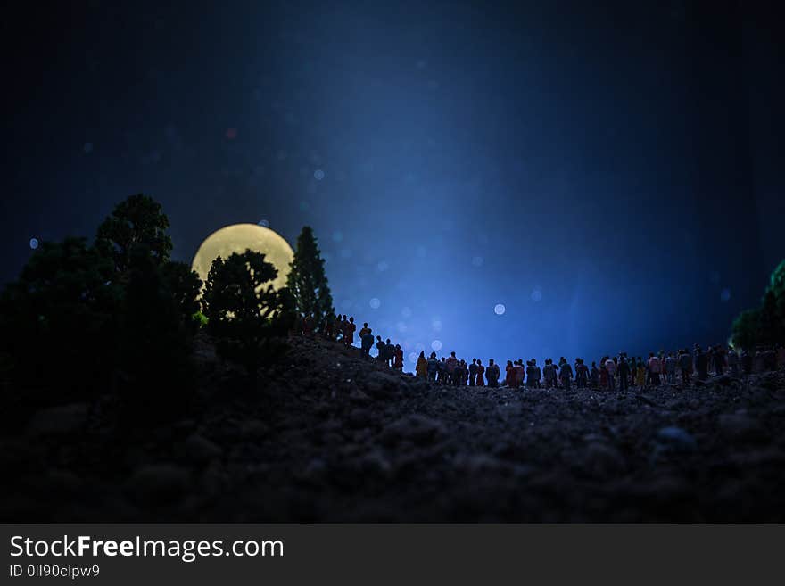 Silhouette of a large crowd of people in forest at night watching at rising big full Moon. Decorated background with night sky with stars, moon and space elements. Selective focus. Surreal world