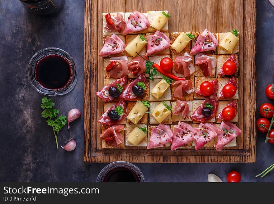 Tasty savory tomato Italian appetizers, or bruschetta, slices of toasted baguette topped with ham, prosciutto on a wooden board.